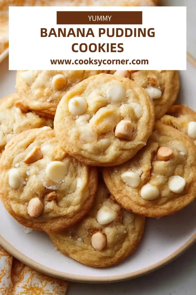 Banana Pudding Cookies stacked on a plate with visible white chocolate chips and vanilla wafer pieces. The cookies look soft, chewy, and golden around the edges.