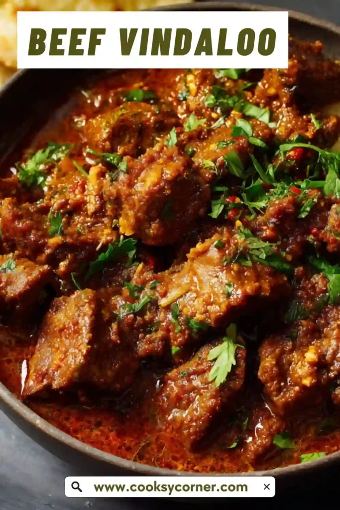 Homemade Beef Vindaloo in a rustic serving bowl with visible tomatoes and fresh herbs. The spicy beef curry looks rich, glossy, and comforting.