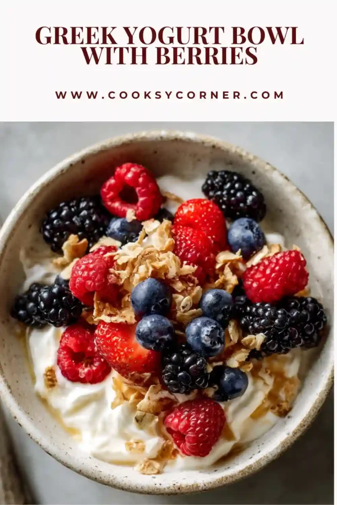 A creamy Greek yogurt bowl with fresh berries and crunchy granola on top. The yogurt looks thick and smooth with vibrant blueberries and raspberries.
