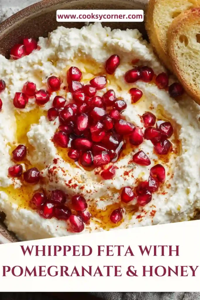 Creamy whipped feta dip topped with pomegranate seeds, pistachios, and honey served on a plate with pita bread. The texture looks smooth and rich with colorful toppings.