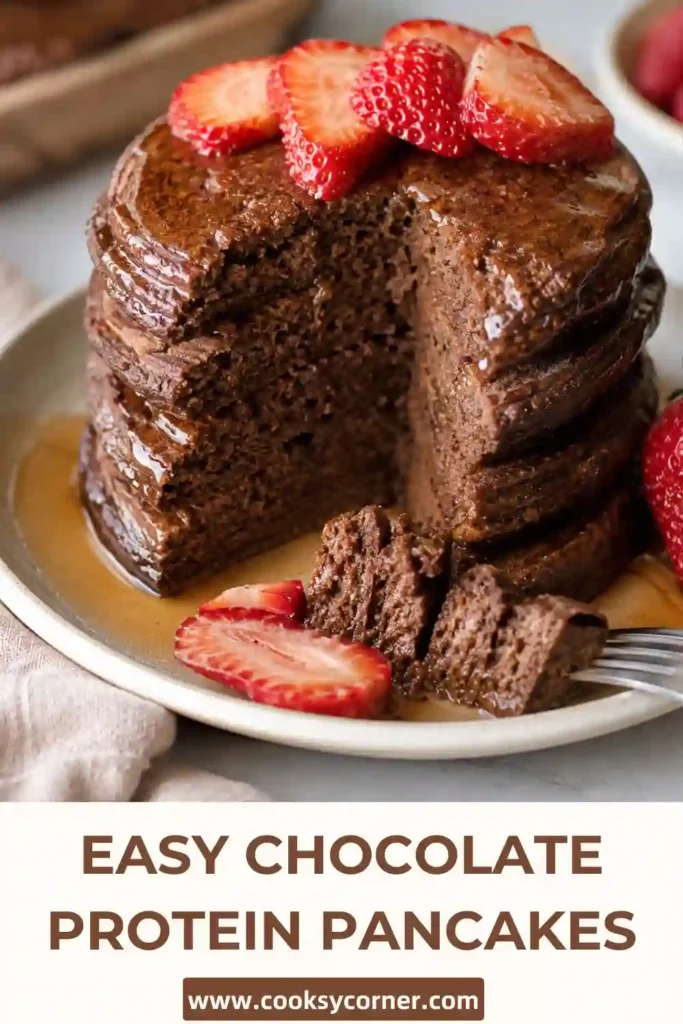 Freshly cooked Chocolate Protein Pancakes stacked on a plate and topped with strawberries and honey. A healthy high-protein breakfast made with bananas, oats, and cocoa powder