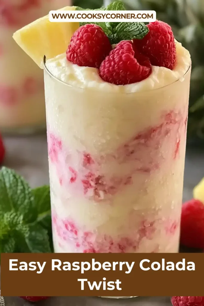 A glass of Easy Raspberry Colada Twist Recipe garnished with fresh raspberries, pineapple wedges, and mint leaves. The tropical drink features vibrant pink hues and a creamy texture.