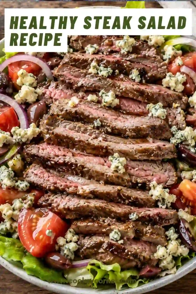 Close-up of sliced steak arranged over romaine lettuce with tomatoes, red onions, and blue cheese. The salad is drizzled with homemade dressing.