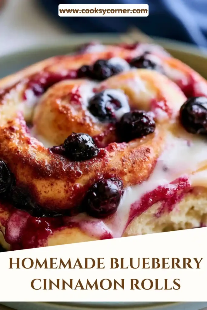 Close-up of a Blueberry Cinnamon Roll featuring swirls of cinnamon filling and fresh blueberries beneath a layer of cream cheese frosting. Soft texture and golden color make this breakfast treat irresistible.
