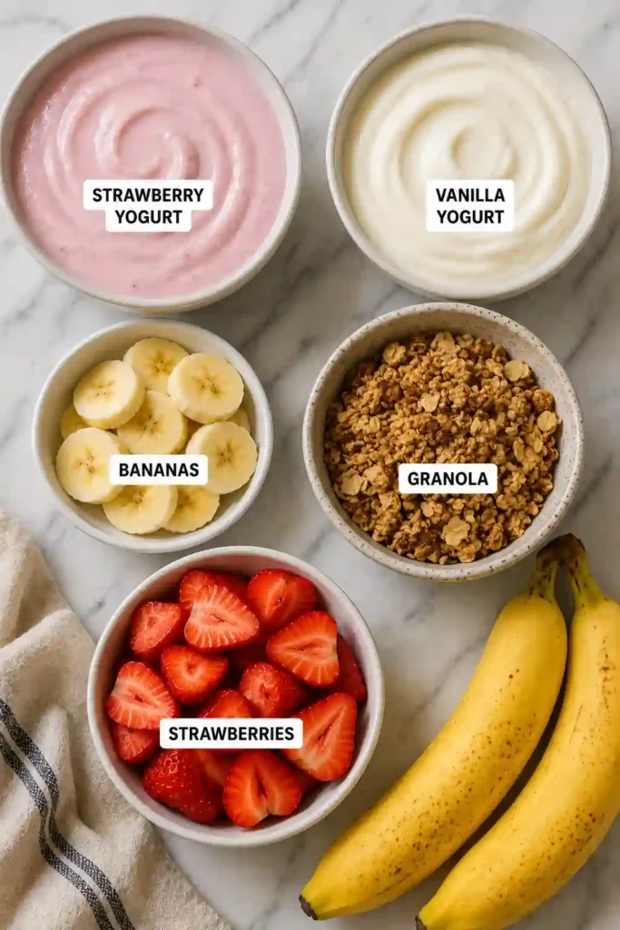Fresh fruit yogurt parfait featuring layers of creamy yogurt, strawberries, bananas, and granola.