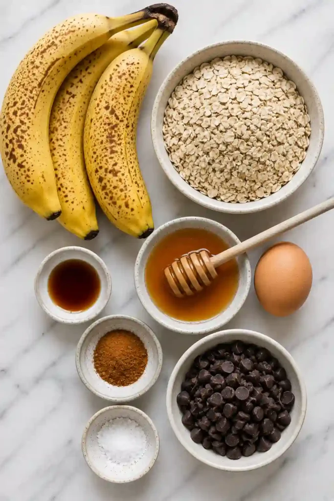 Homemade Banana Oatmeal Cookies stacked on a serving plate with fresh bananas and oats nearby. The cookies have a rustic homemade appearance with melted chocolate chips.