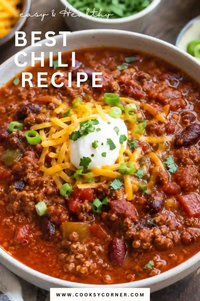 A bowl of the Best Chili Recipe topped with shredded cheddar cheese, chopped green onions, and fresh cilantro. This hearty homemade ground beef chili is thick, rich, and perfect for comfort food lovers.