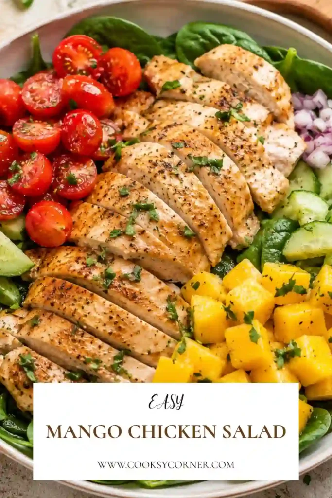 A fresh Mango Chicken Salad served in a large bowl with sliced chicken, ripe mango, romaine lettuce, spinach, cucumbers, and cherry tomatoes. The colorful salad is topped with homemade honey lemon dressing.