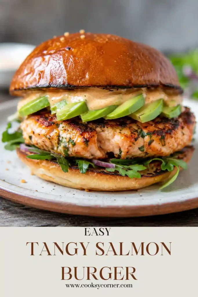 A juicy Tangy Salmon Burger served on a toasted bun with fresh lettuce and tomato. The golden salmon patty is perfectly cooked and ready for a delicious meal.