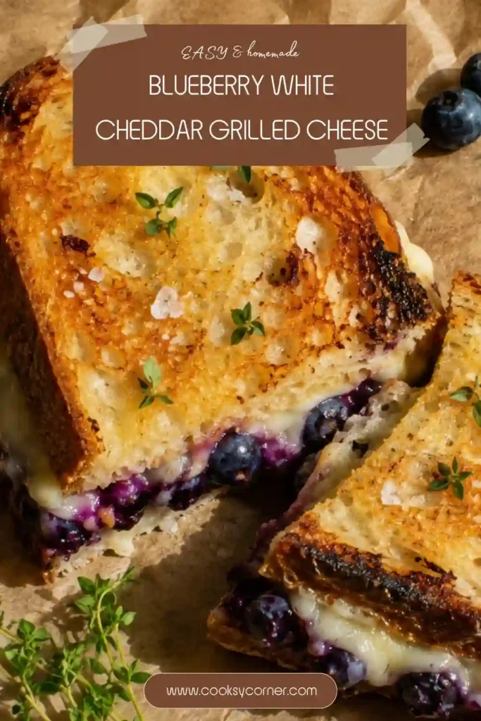 Blueberry grilled cheese sandwich with thick purple blueberry jam and gooey white cheddar and mozzarella between crisp buttery sourdough. The sandwich is sliced in half to reveal the colorful melted center.