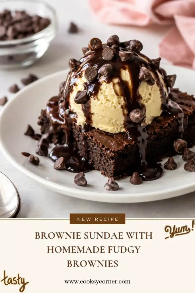 Brownie Sundae with a thick fudgy chocolate brownie topped with creamy ice cream, glossy chocolate sauce, and mini chocolate chips. Whipped cream and a cherry add a classic sundae finish.