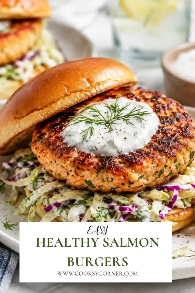 Close-up of homemade healthy salmon burgers topped with fresh herbs and served alongside creamy Greek yogurt cabbage slaw. A fresh and protein-rich seafood meal.