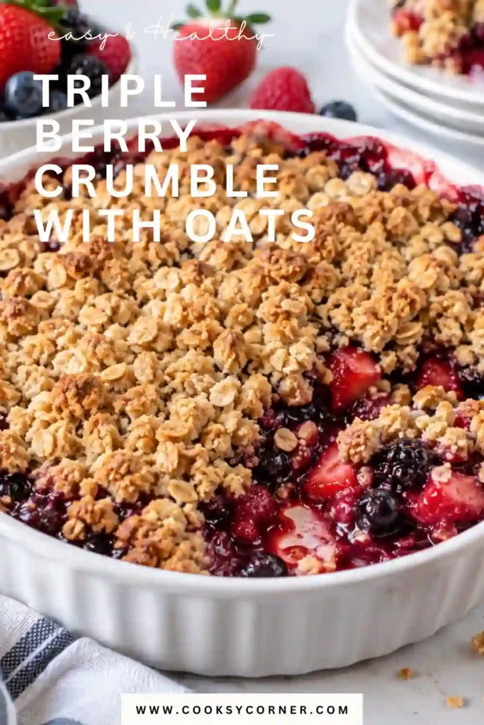 Warm Triple Berry Crumble With Oats featuring a bubbling berry filling beneath crunchy golden oat crumbs. A scoop of vanilla ice cream melts gently over the freshly baked dessert.