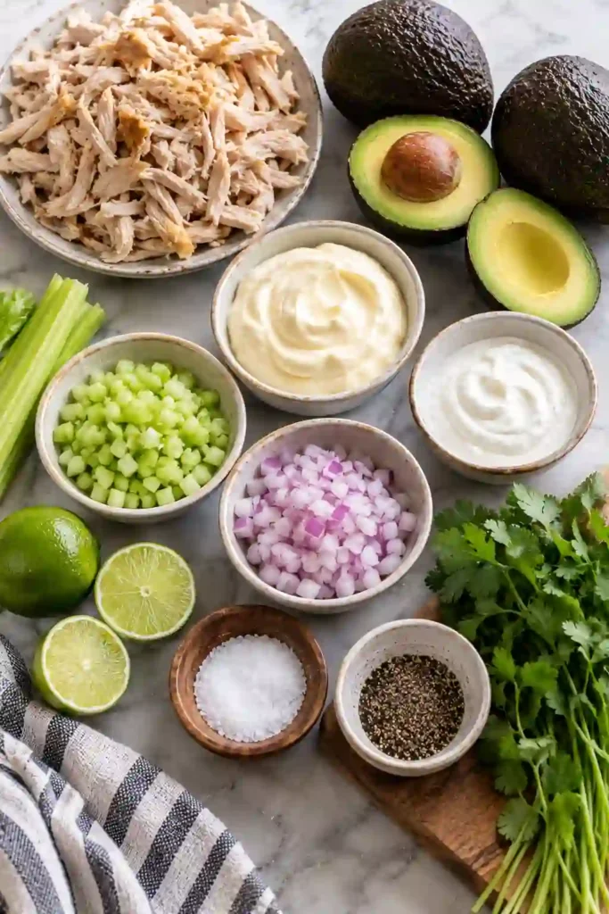 Homemade Creamy Avocado Chicken Salad served in a bowl with fresh lime and avocado. The easy chicken salad has a creamy texture with visible pieces of chicken, celery, cilantro, and avocado.