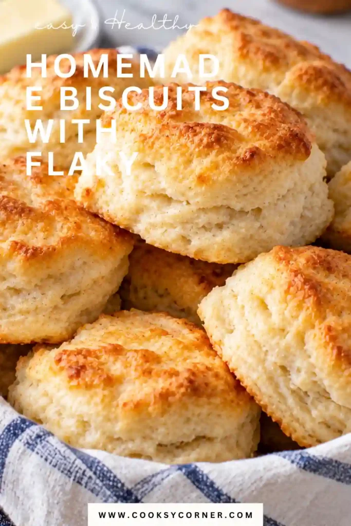A basket filled with golden homemade biscuits resting on a cloth napkin. The biscuits have lightly browned tops and fluffy, layered sides.