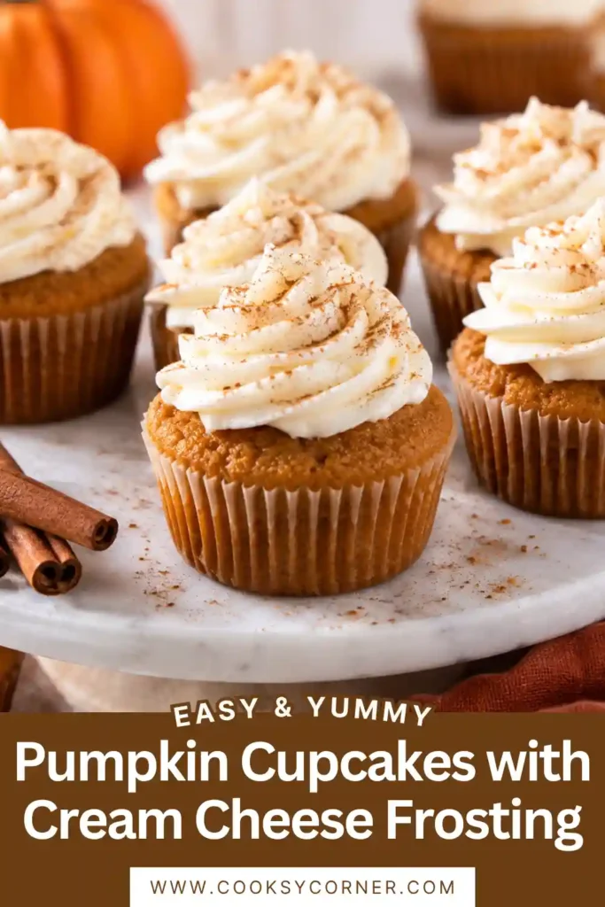 Pumpkin spice cupcakes with cream cheese frosting displayed on a rustic autumn dessert table. Small pumpkins and warm seasonal decorations surround the golden cupcakes, creating a cozy fall baking scene.