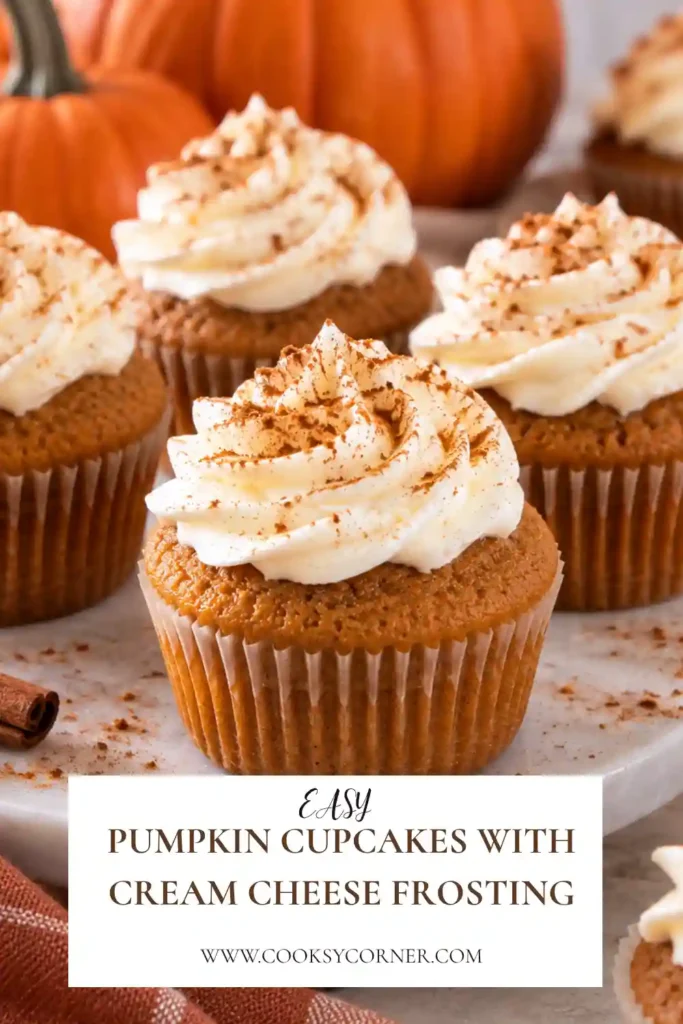 Pumpkin cupcakes with cream cheese frosting arranged on a serving plate with generous swirls of creamy white frosting. The golden-orange cupcakes have a soft, moist texture and a delicate dusting of cinnamon.