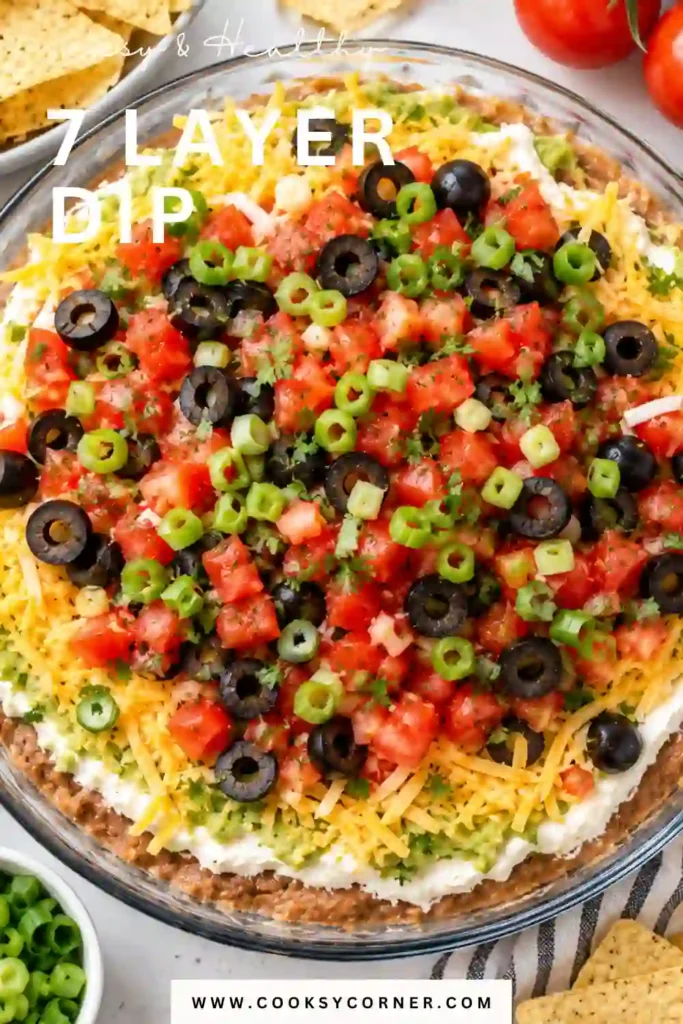 Mexican-inspired layered bean dip with guacamole, sour cream, shredded cheddar, tomatoes, olives, and green onions. The creamy taco dip is ready to serve with crunchy tortilla chips.